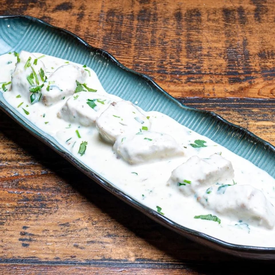 Chicken malai boti, a creamy white chicken dish with green herbs, served in a blue dish.