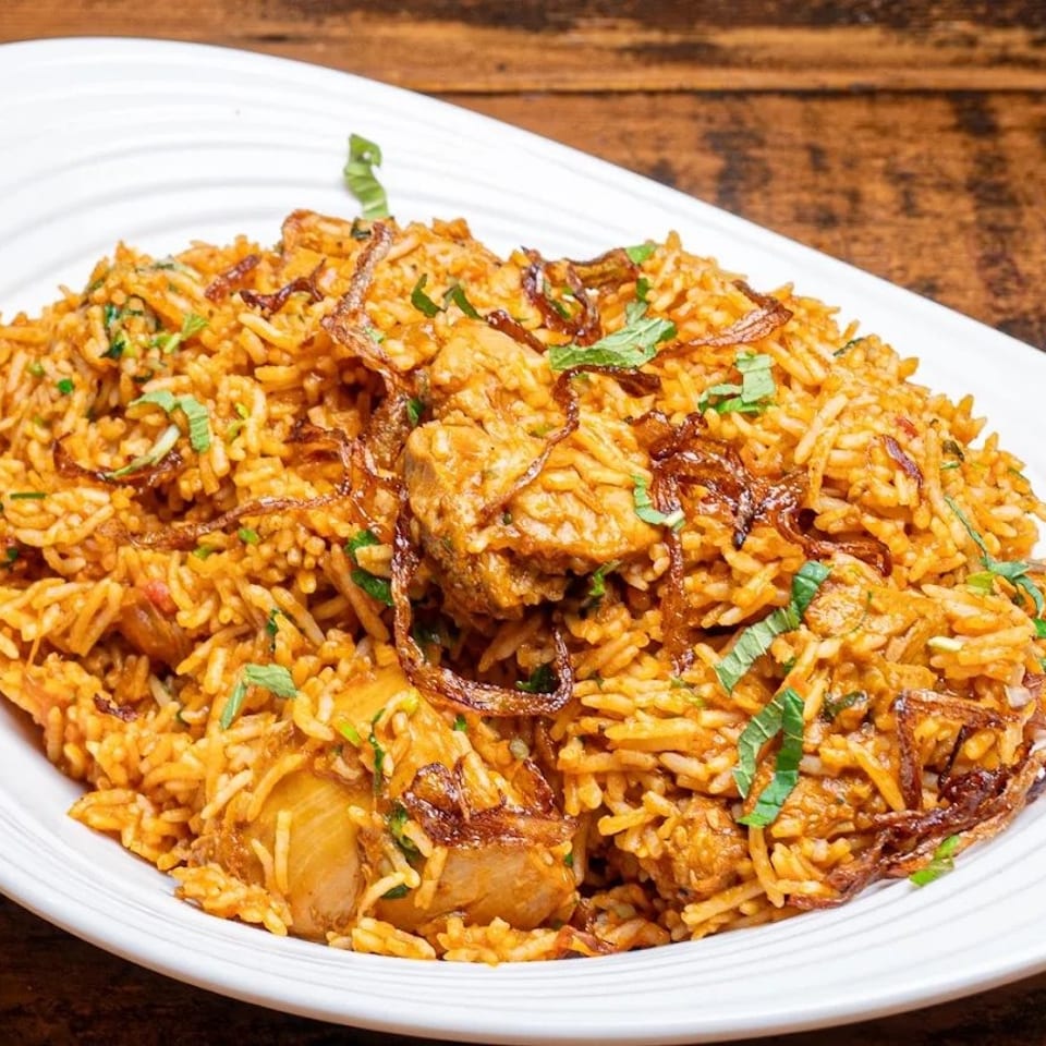A large white platter filled with chicken biryani, garnished with fried onions and fresh mint.
