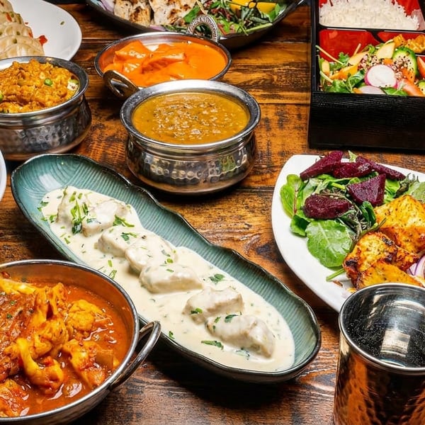 A vibrant spread of Indian dishes including curries, rice, naan, and paneer tikka on a wooden table.